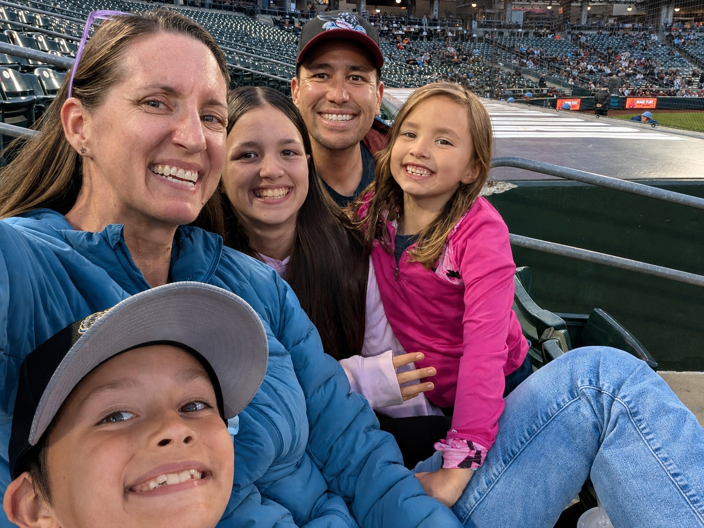 Kelly and Mike with their three children smiling together at a baseball game